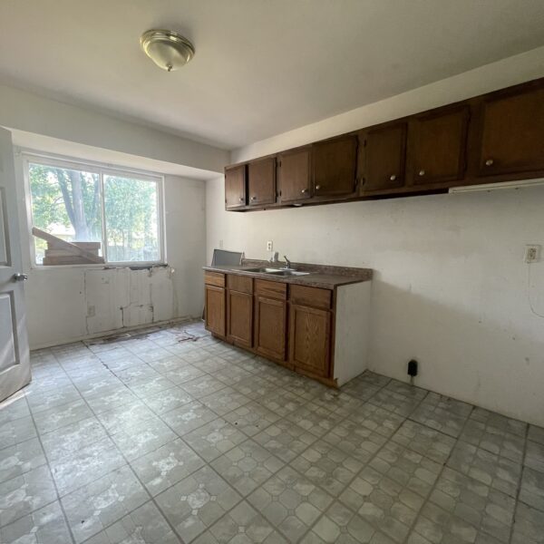 An empty kitchen with cabinets and a window.