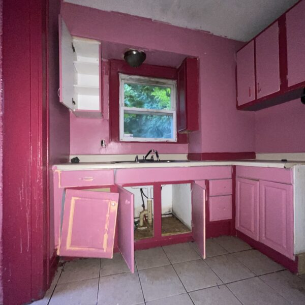 A pink kitchen with white cabinets and a sink.